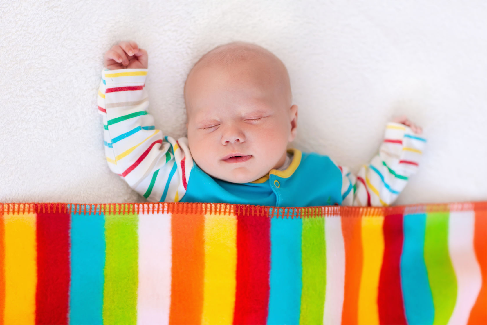 bebé dormido en la cuna tapado con una manta de colores